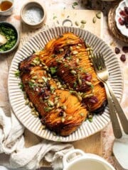 Hasselback butternut squash on a striped platter, topped with dried cranberries, toasted pepitas, and fresh parsley.