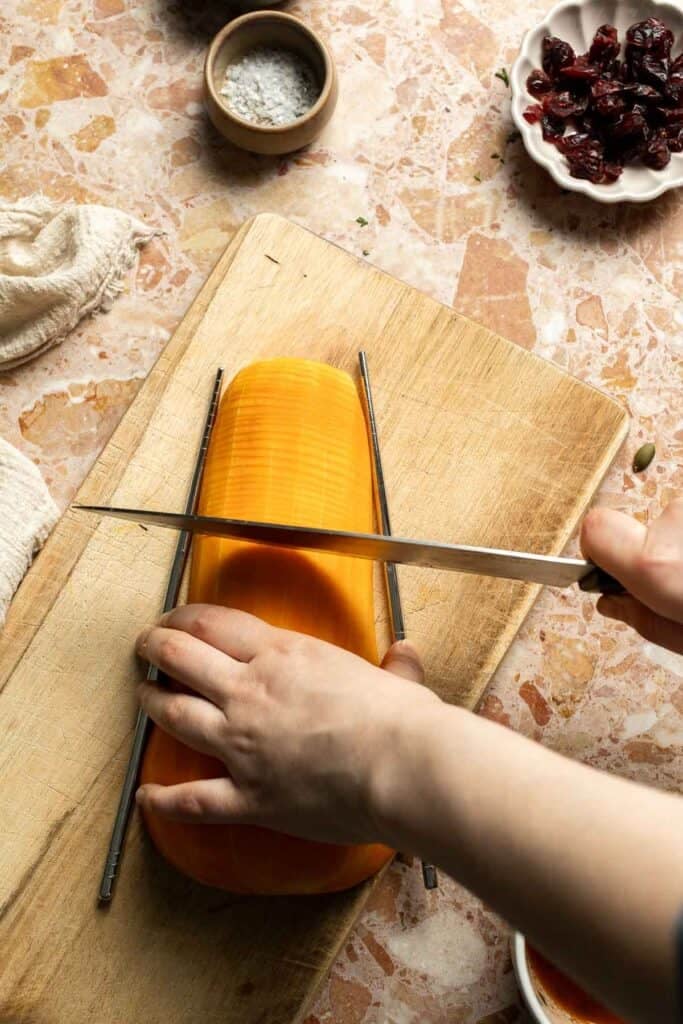 Slicing a butternut squash half into thin hasselback cuts with chopsticks on either side to guide the knife.