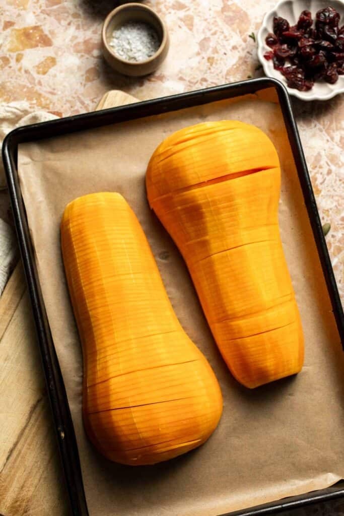 Sliced butternut squash halves cut side up on a parchment-lined baking sheet.