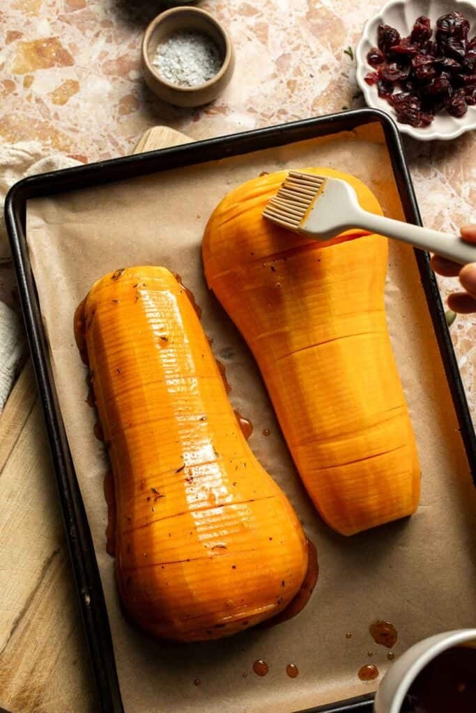 Brushing maple butter over the hasselback butternut squash halves.