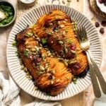 Hasselback butternut squash on a striped platter, topped with dried cranberries, toasted pepitas, and fresh parsley.