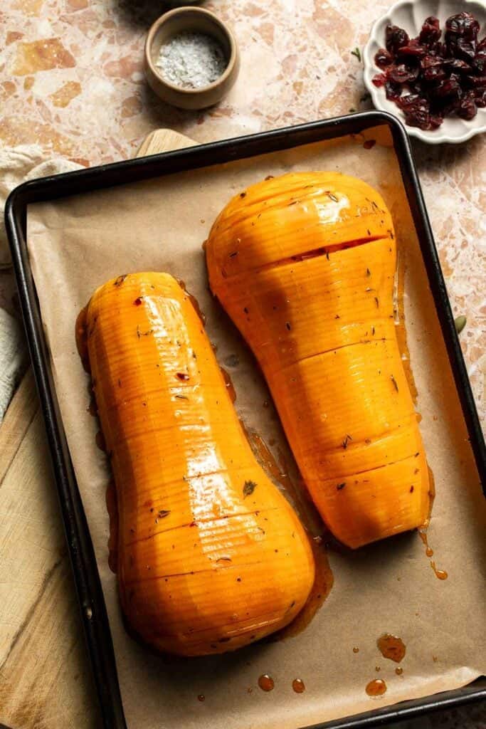 Hasselback butternut squash glazed with maple butter on a baking sheet, ready to roast.
