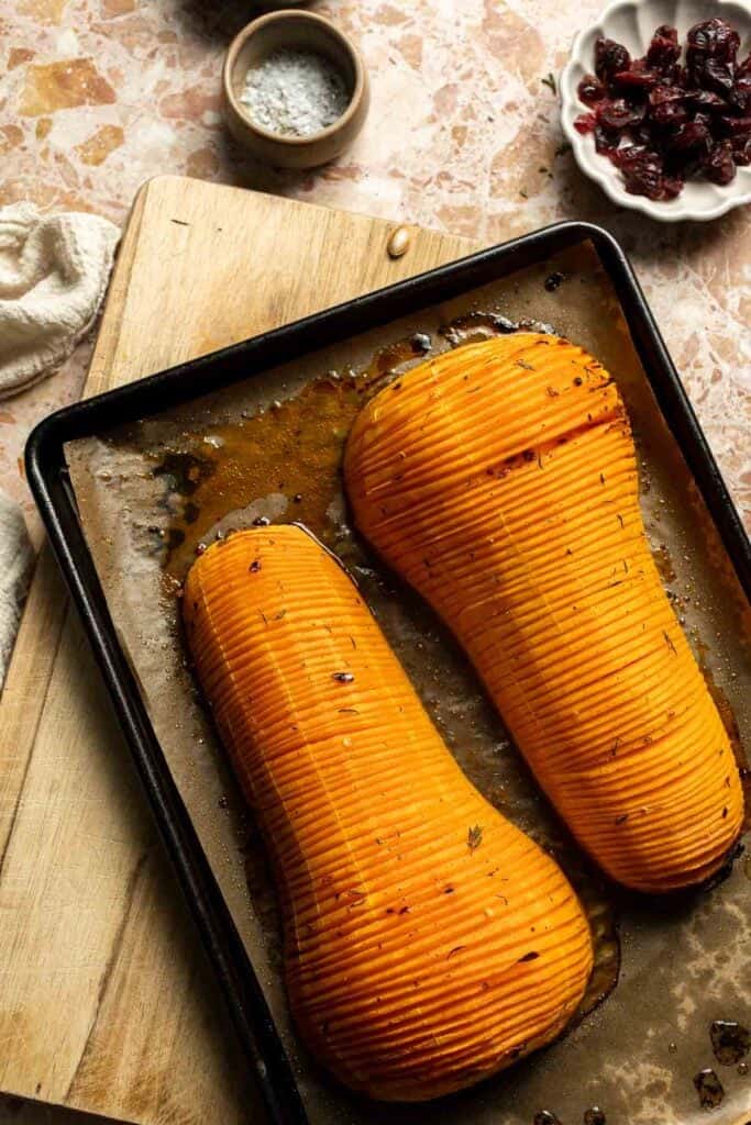 Hasselback butternut squash partway through roasting, with the slices beginning to open and pan juices collecting on the sheet.