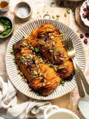 Hasselback butternut squash on a striped platter, topped with dried cranberries, toasted pepitas, and fresh parsley.