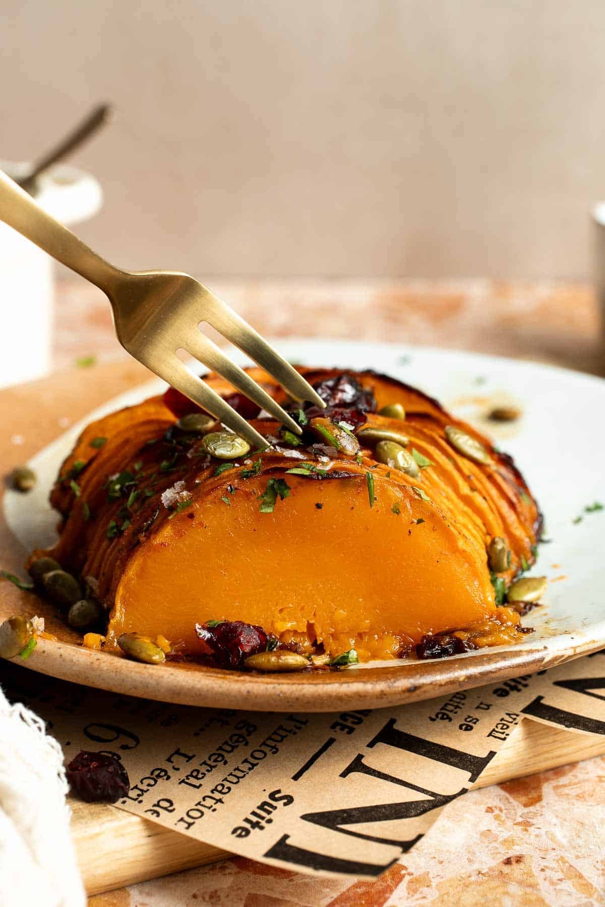Fork cutting into a tender slice of hasselback butternut squash on a plate, showing the soft orange flesh.