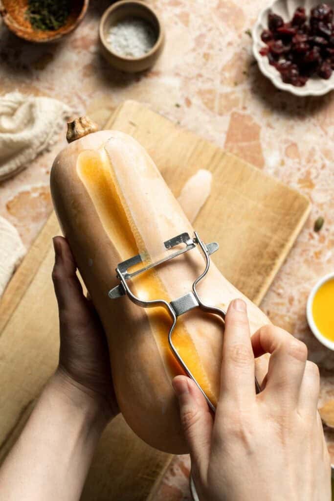 Peeling a butternut squash with a vegetable peeler.