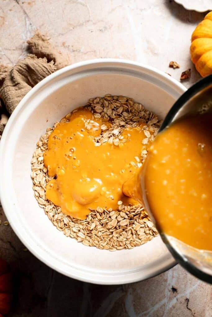 Pumpkin mixture being poured into the bowl of dry oats