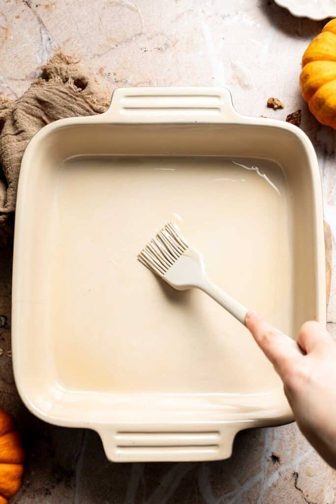 Square baking dish being greased with a pastry brush