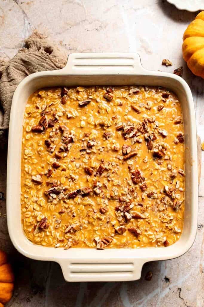 Chopped pecans sprinkled over unbaked pumpkin oatmeal batter in a baking dish