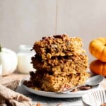 Stack of pumpkin baked oatmeal squares with pecans and maple syrup being drizzled over the top