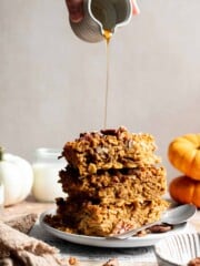 Stack of pumpkin baked oatmeal squares with pecans and maple syrup being drizzled over the top