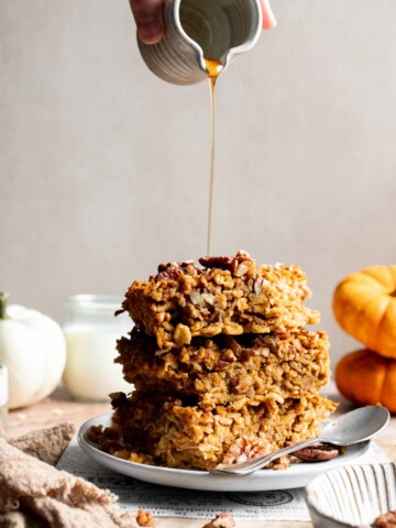 Stack of pumpkin baked oatmeal squares with pecans and maple syrup being drizzled over the top