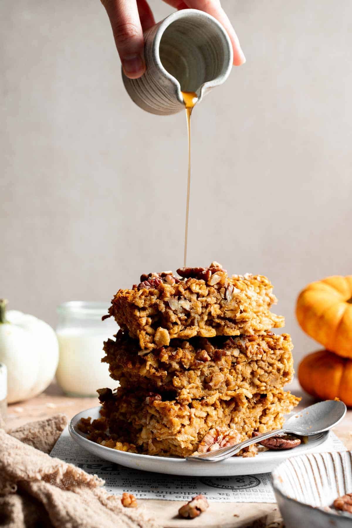 Stack of pumpkin baked oatmeal squares with pecans and maple syrup being drizzled over the top