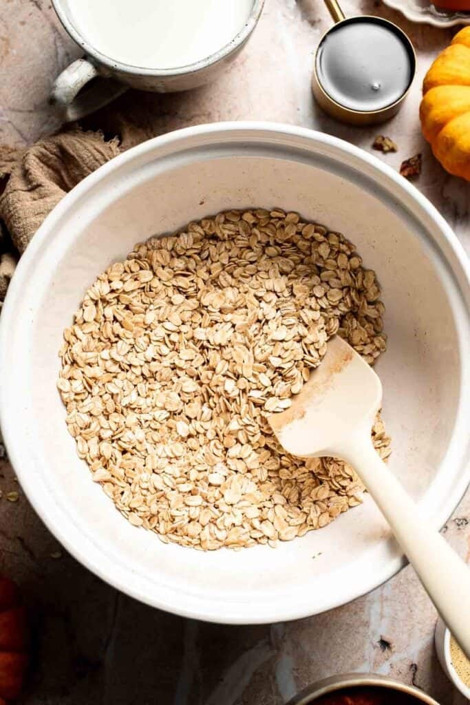 Rolled oats and spices stirred together with a spatula in a large mixing bowl