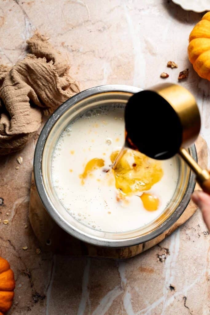 Milk and eggs in a mixing bowl with maple syrup being poured in