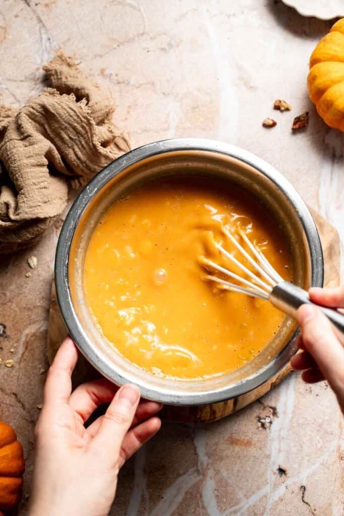 Pumpkin puree and wet ingredients being whisked together in a mixing bowl