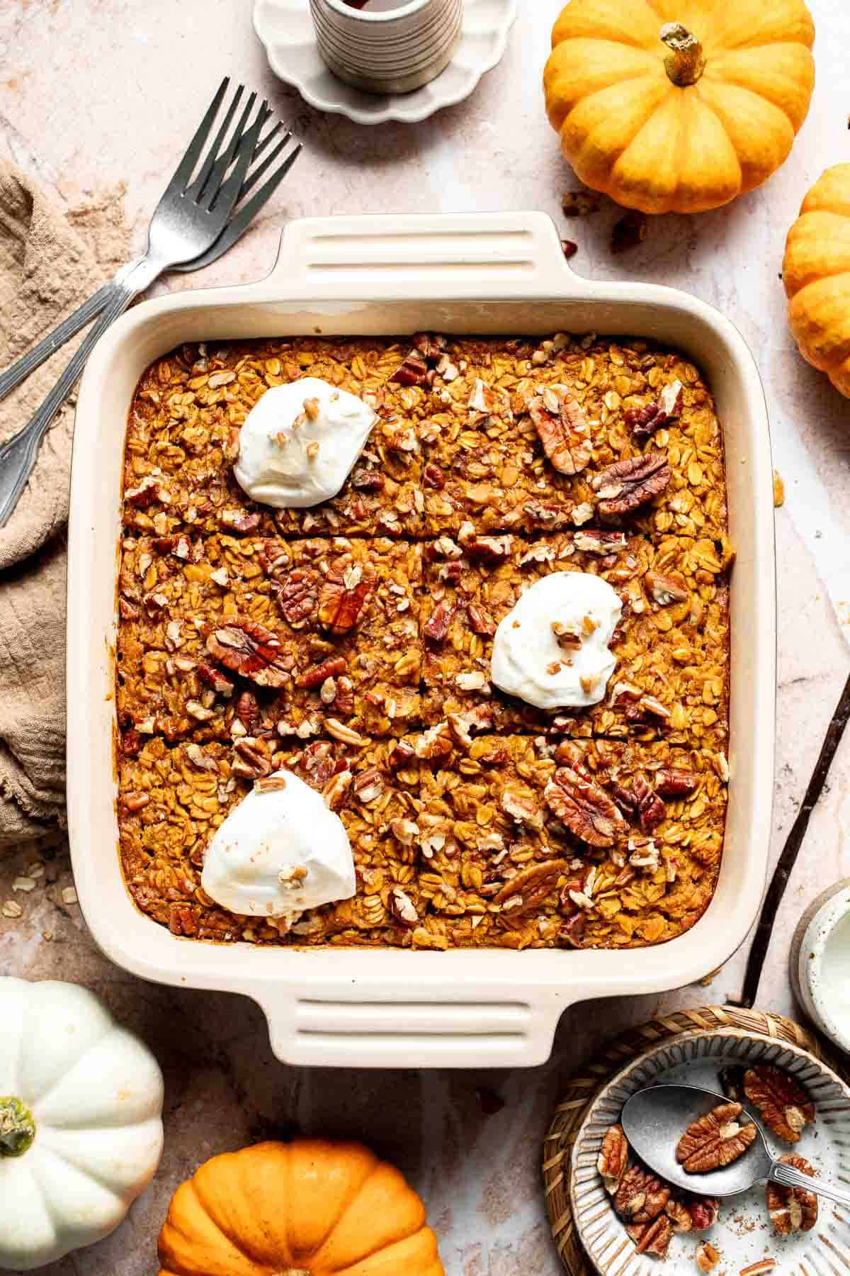 Overhead view of pumpkin baked oatmeal in a baking dish with a fork, mini pumpkins, and Greek yogurt on top