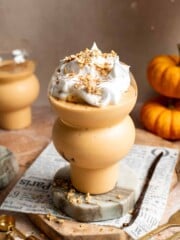 Pumpkin pie smoothie with whipped cream and granola on a marble stand, surrounded by mini pumpkins.