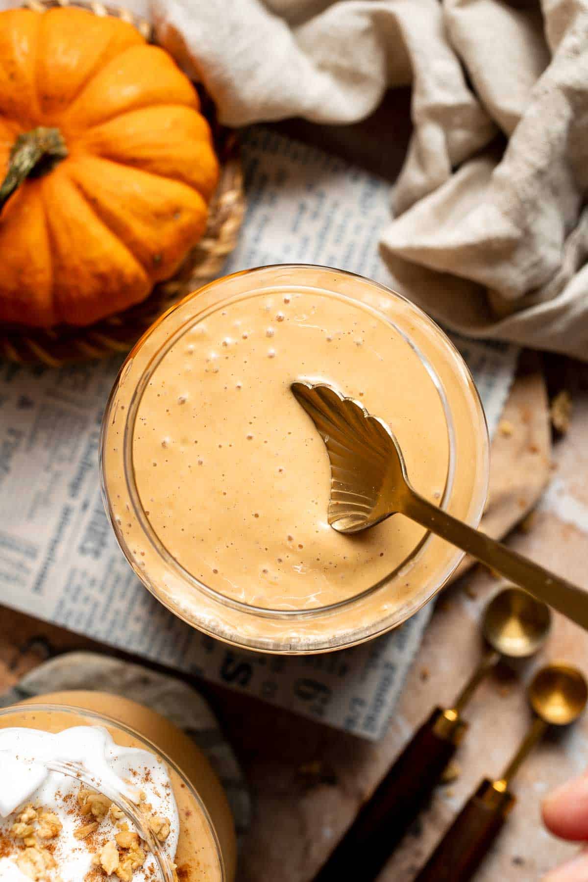 Overhead view of a pumpkin pie smoothie with a gold spoon, mini pumpkins, and a linen napkin.