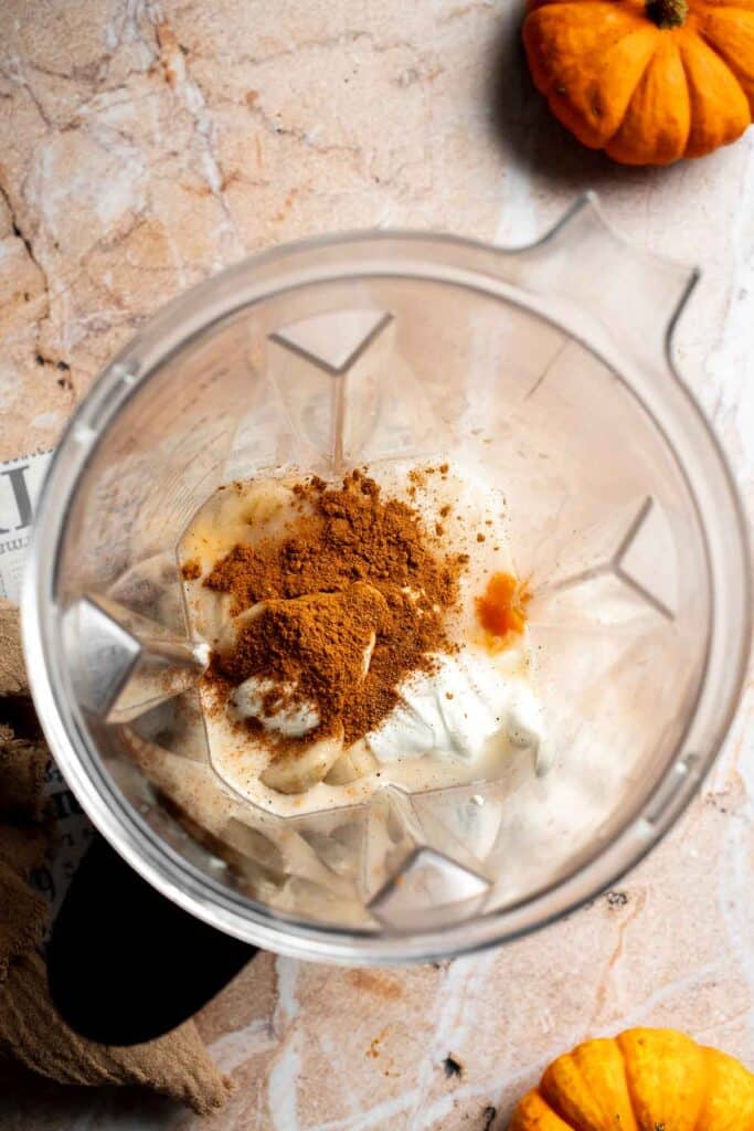 Pumpkin puree, banana, Greek yogurt, and pumpkin pie spice added to a blender, shown from above.