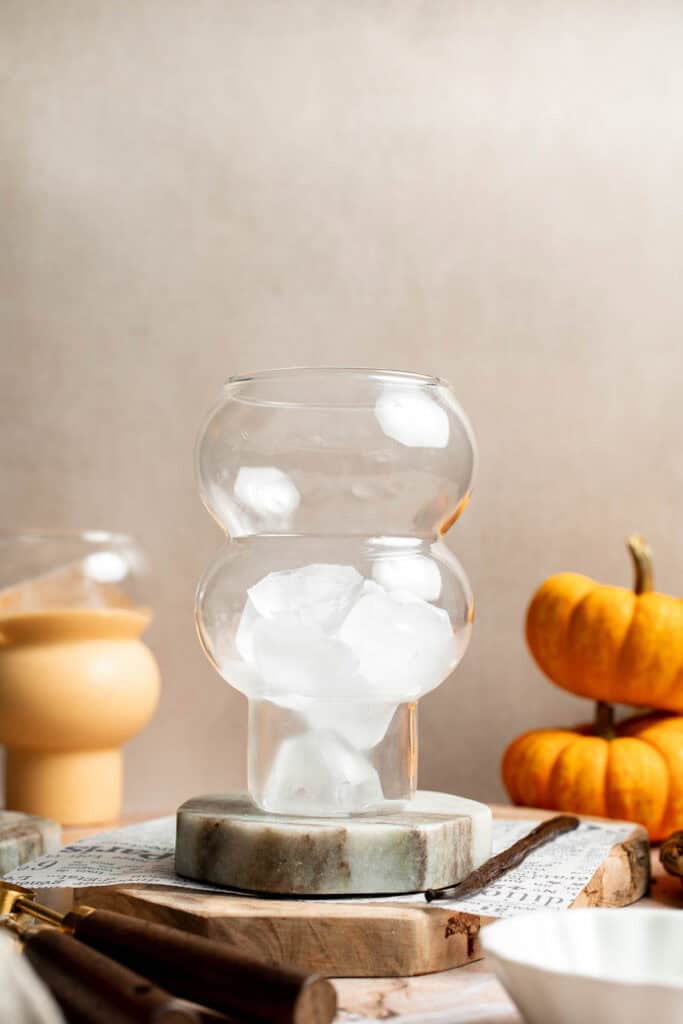 Ice cubes in a stacked glass before pouring the pumpkin smoothie, with mini pumpkins in the background.