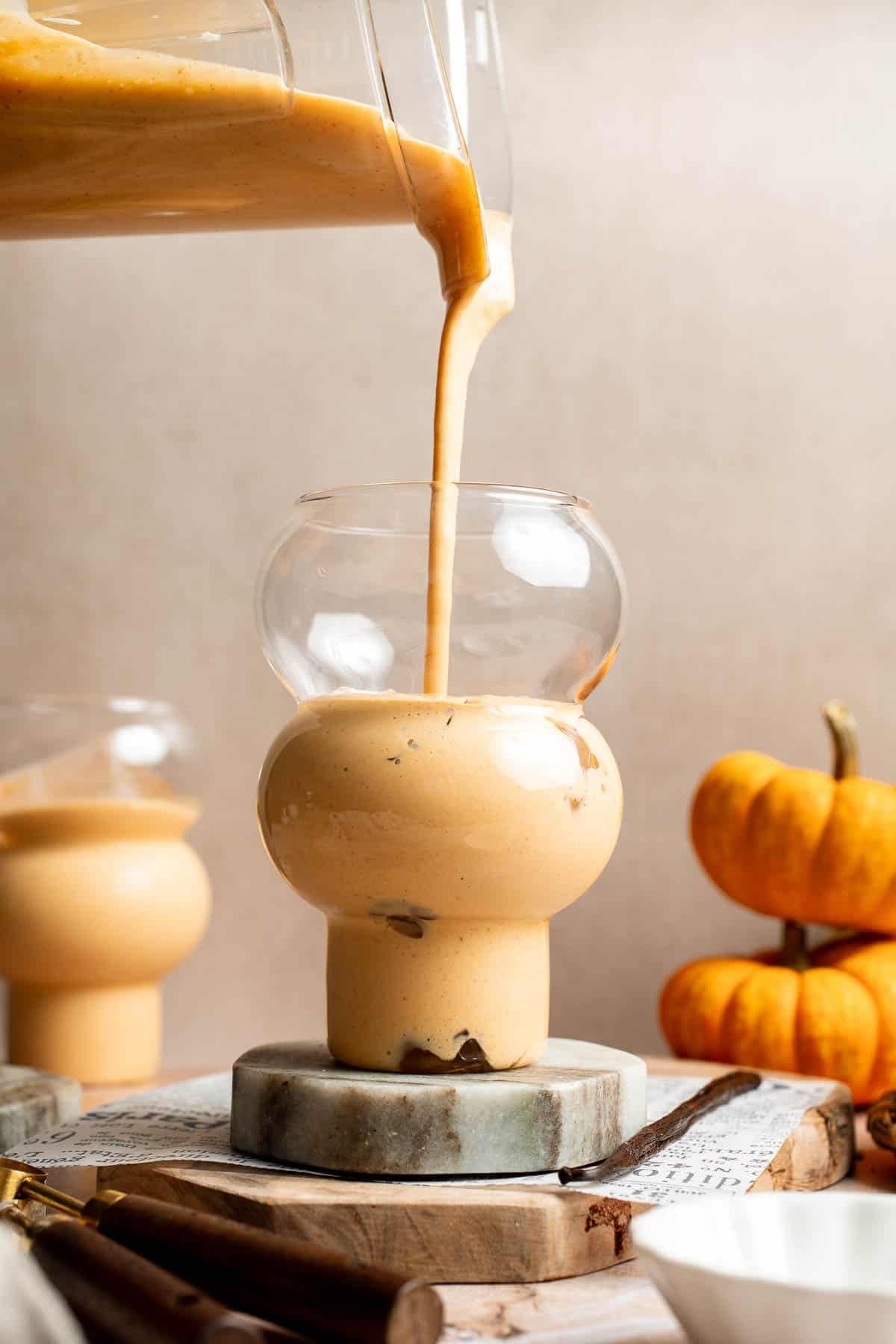 Pouring creamy pumpkin pie smoothie from a blender into a stacked glass.
