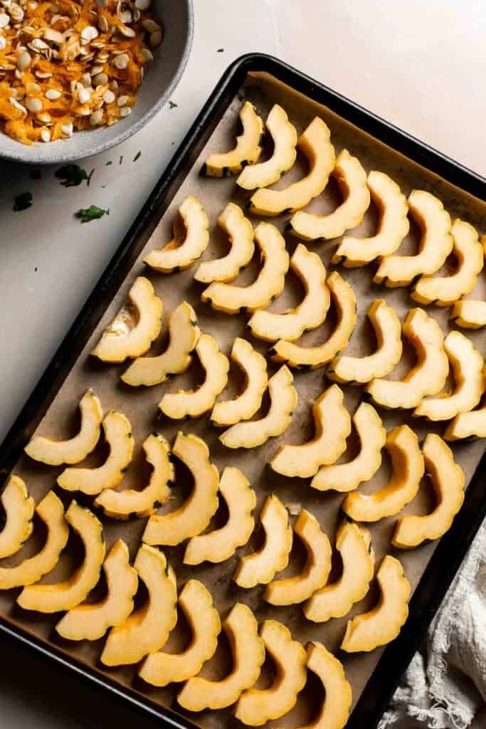 Delicata squash slices spread in a single layer on a parchment-lined baking sheet.