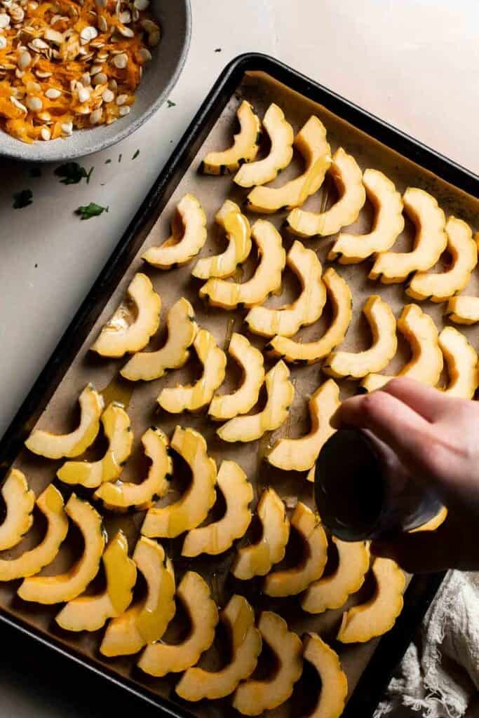 Drizzling olive oil over the delicata squash slices on the baking sheet.
