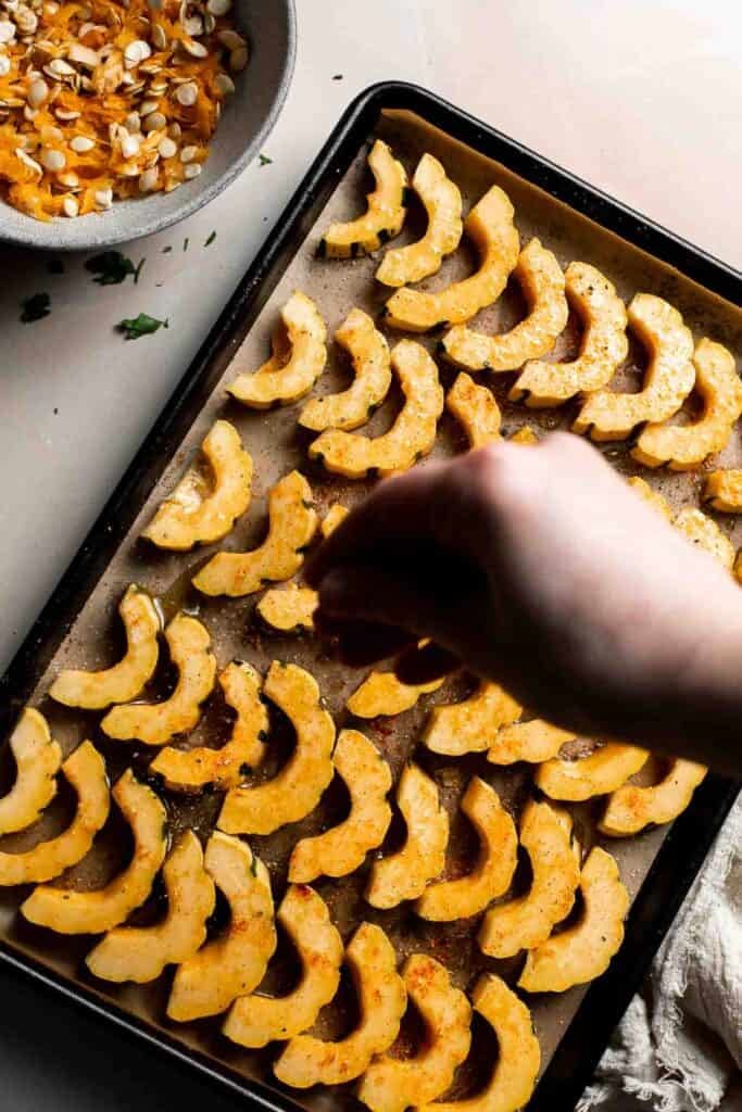 Sprinkling thyme, salt, and pepper over the seasoned delicata squash slices.