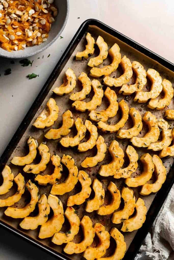 Seasoned delicata squash slices on a baking sheet, ready to go in the oven.