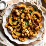 Savory roasted delicata squash in a scalloped bowl, garnished with fresh parsley and served with a gold fork.