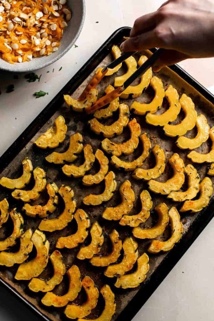 Flipping the delicata squash slices halfway through roasting with tongs.