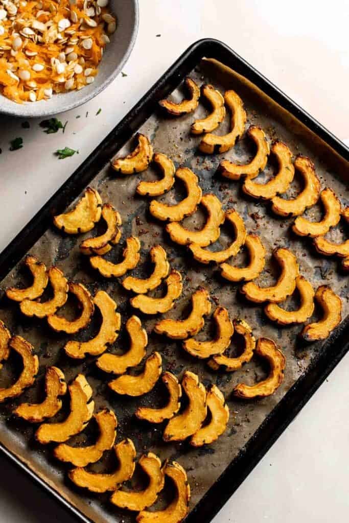 Fully roasted delicata squash slices with deeply golden brown, caramelized edges on the baking sheet.