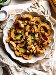 Savory roasted delicata squash in a scalloped bowl, garnished with fresh parsley and served with a gold fork.