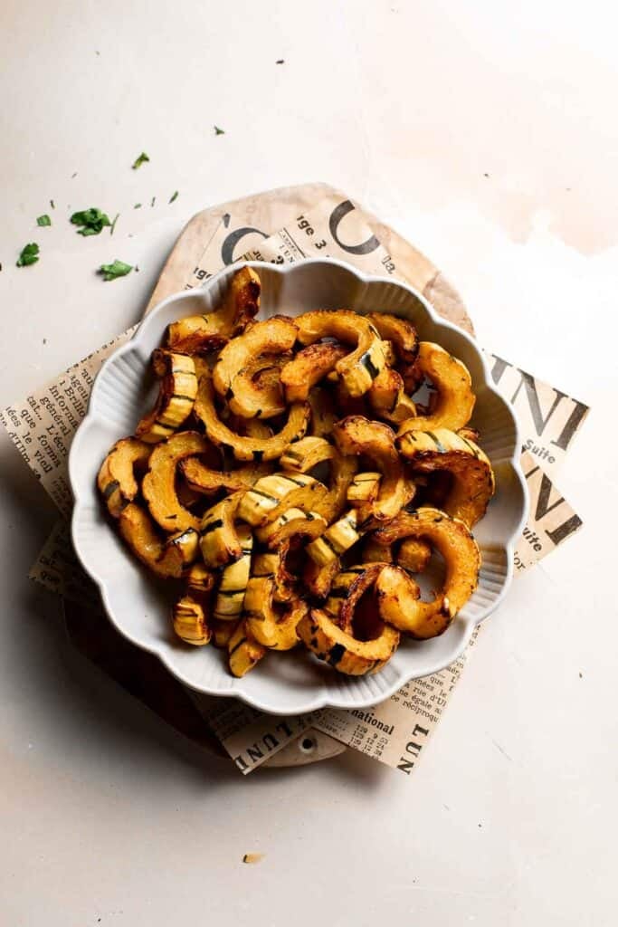 Roasted delicata squash in a scalloped white bowl on a cutting board.