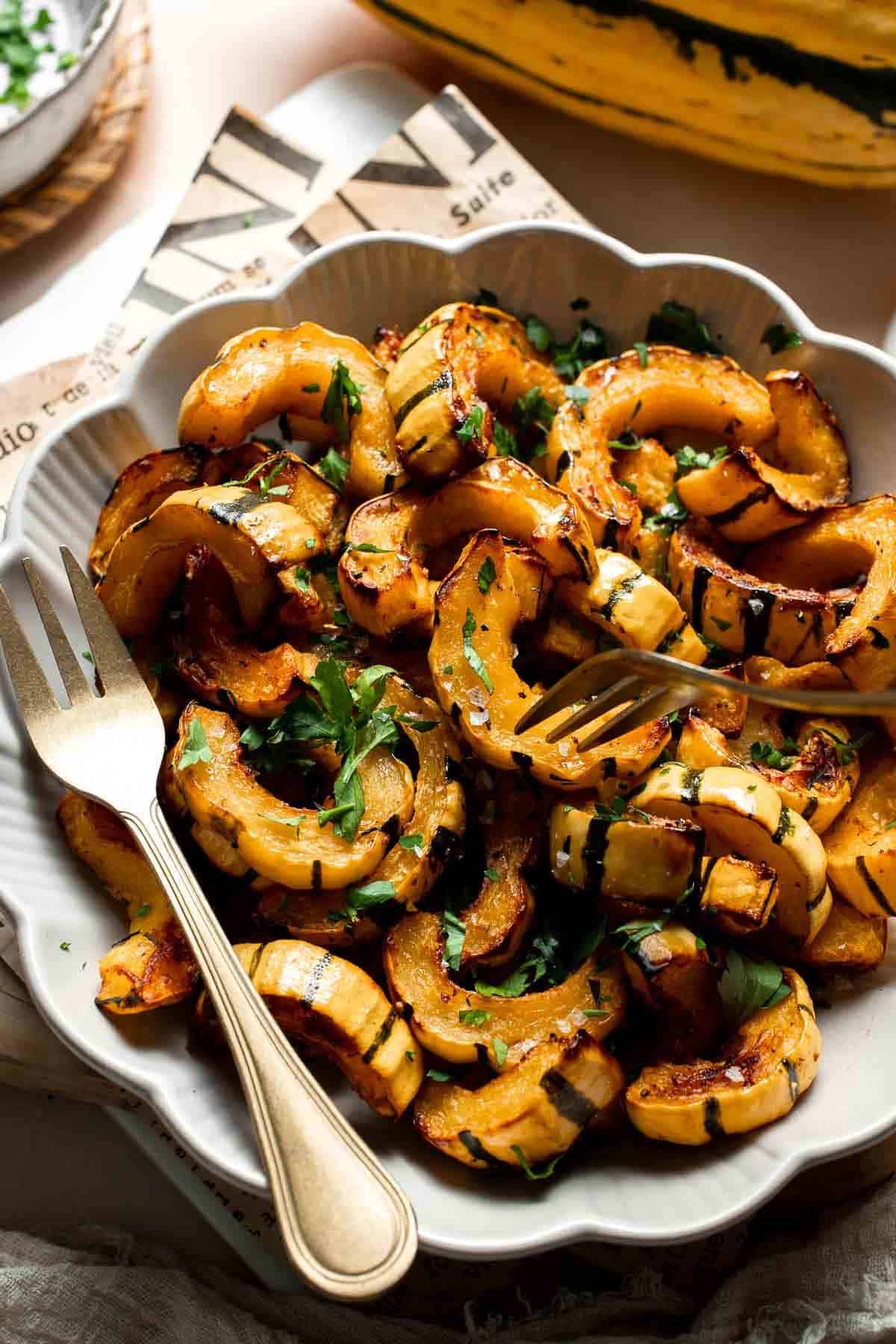 Close-up of roasted delicata squash with caramelized edges and fresh parsley, served with a gold fork.
