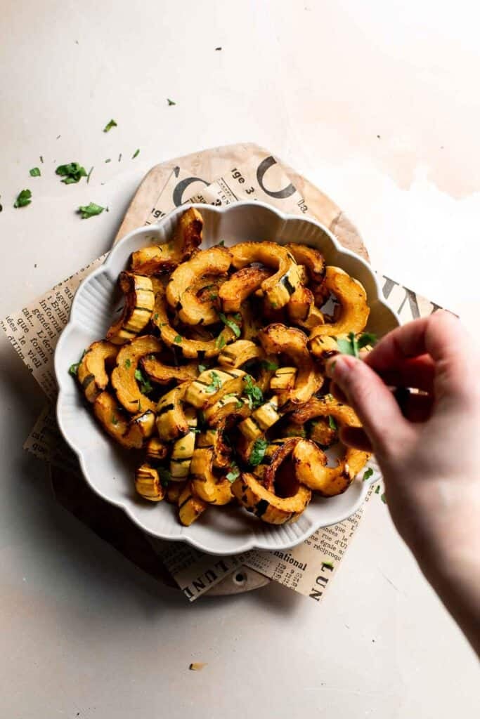 Sprinkling chopped fresh parsley over the roasted delicata squash.