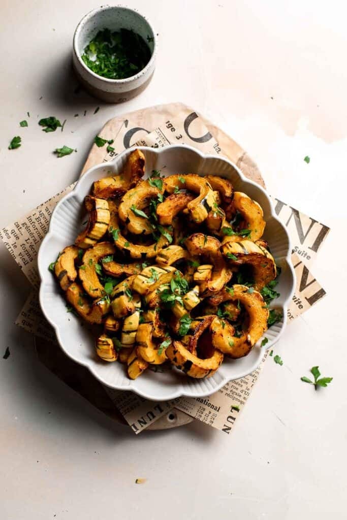 Roasted delicata squash garnished with chopped fresh parsley, with a small bowl of parsley nearby.