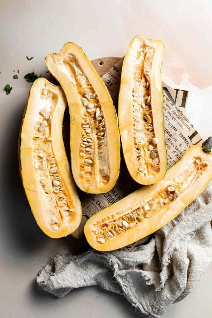 Delicata squash cut in half lengthwise, showing the seeds and stringy flesh inside.