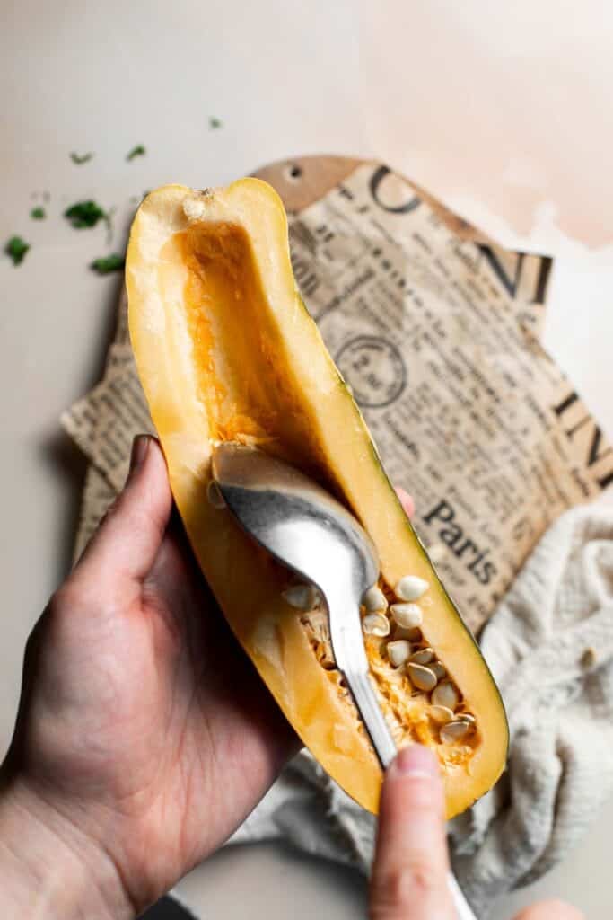Scooping the seeds out of a delicata squash half with a spoon.