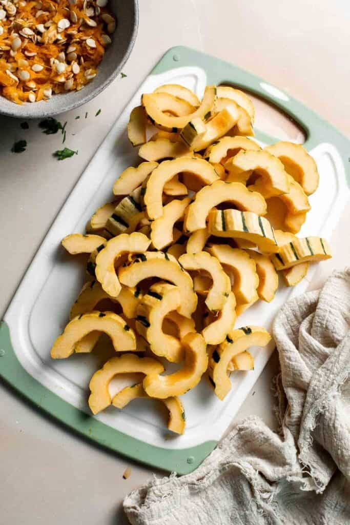 Sliced delicata squash half-moons on a cutting board, ready to roast.