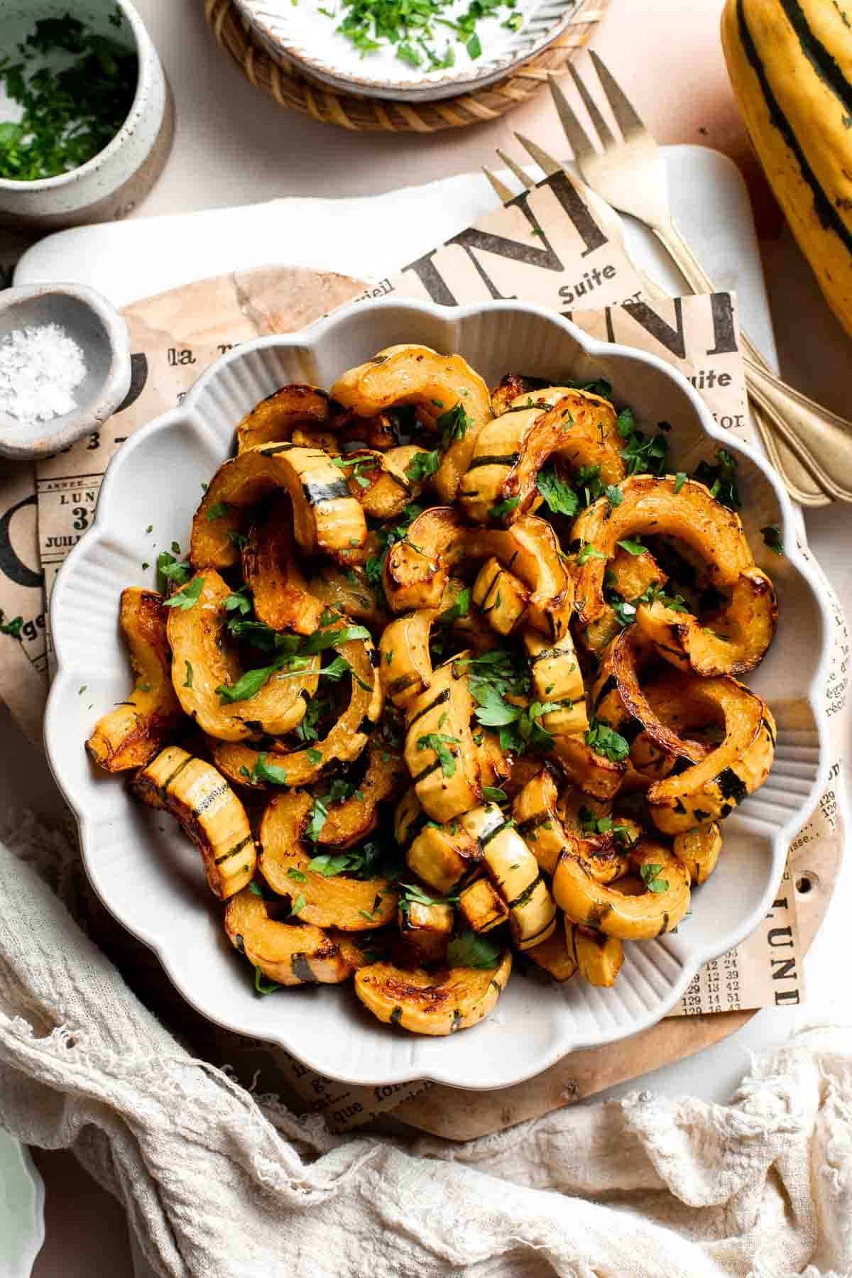 Savory roasted delicata squash in a scalloped bowl, garnished with fresh parsley and served with a gold fork.