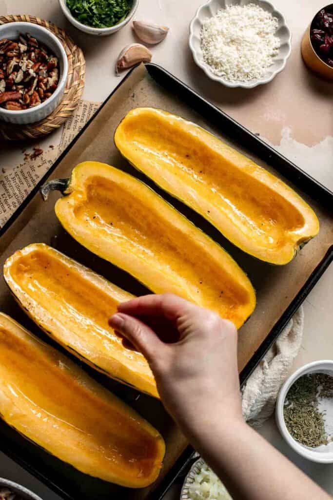 Sprinkling salt and pepper over the oiled delicata squash halves.