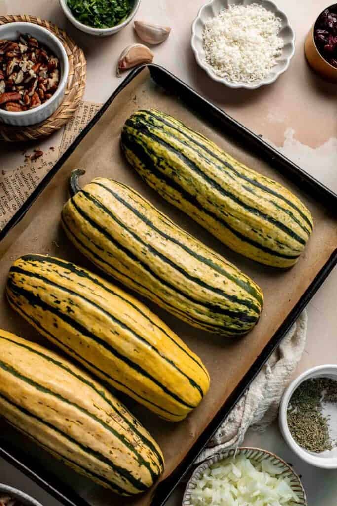 Delicata squash halves turned cut-side down on the baking sheet, ready to roast.