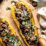 Baked stuffed delicata squash with wild rice, cranberries, pecans, and Parmesan, garnished with fresh parsley on a wooden board.