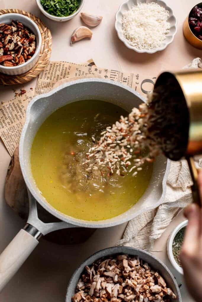 Pouring wild rice blend into the saucepan of vegetable broth.