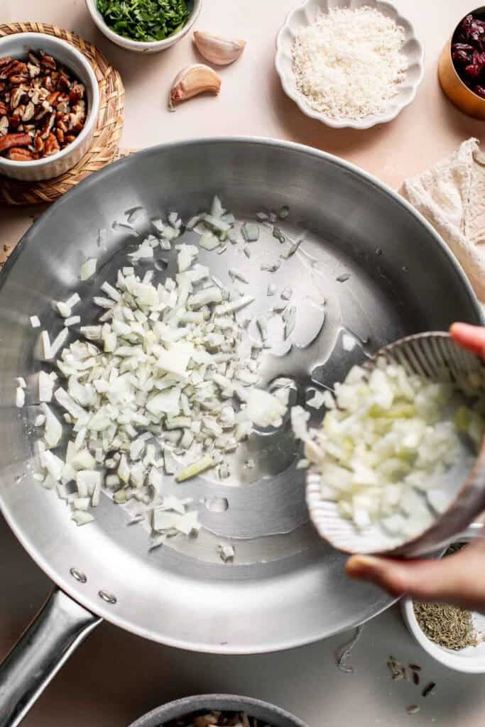 Adding diced onion to a stainless steel skillet.