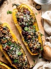 Baked stuffed delicata squash with wild rice, cranberries, pecans, and Parmesan, garnished with fresh parsley on a wooden board.