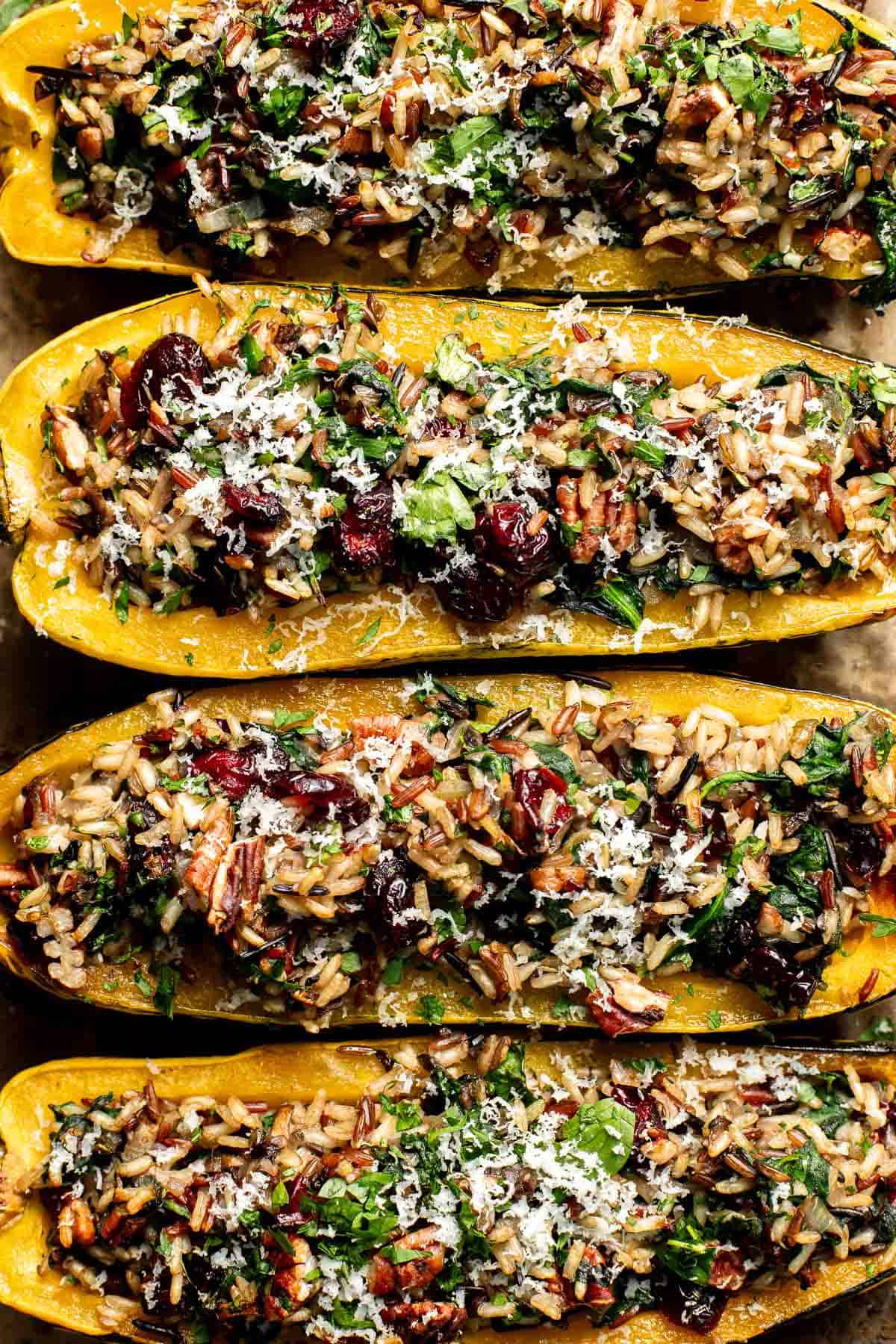 Overhead close-up of four stuffed delicata squash halves topped with cranberries, pecans, Parmesan, and parsley.
