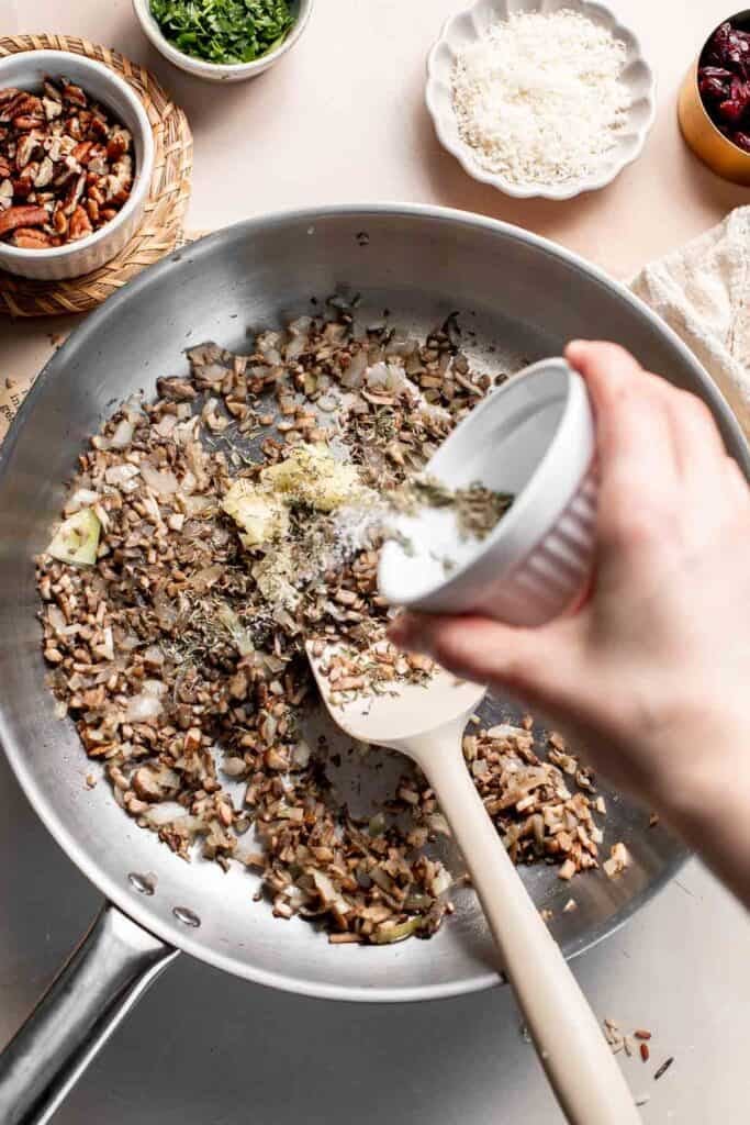Sprinkling dried herbs and salt over the mushroom mixture.